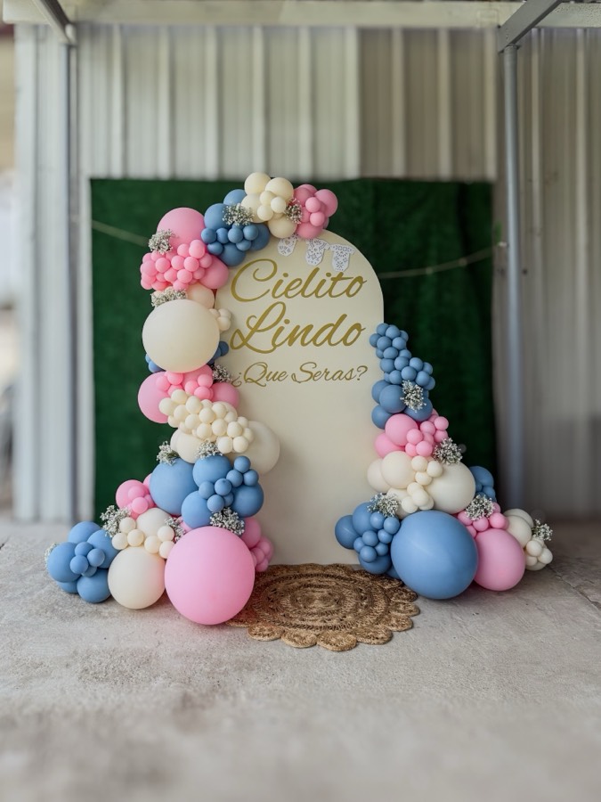 Cream arch backdrop reading “Cielito Lindo ¿Que Seras?” in gold script, with pink, dusty blue and cream balloon garlands accented with baby's breath.