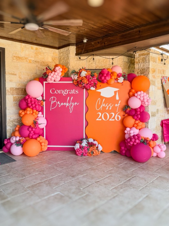 A hot-pink framed panel and an orange scalloped panel reading “Congrats Brooklyn” and “Class of 2026”, flanked by pink and orange balloon columns with hydrangea accents.